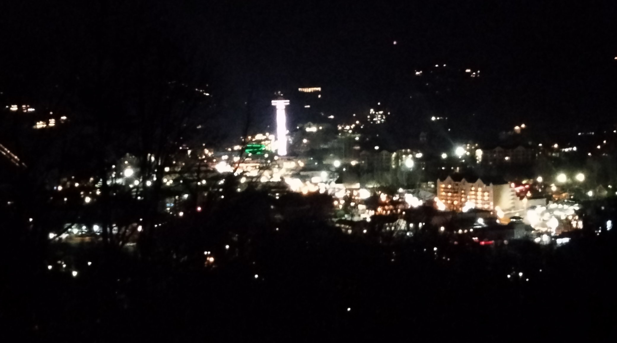 A picture of a view from the Smoky Mountain Bypass Overlook. Gatlinberg, a tourist city, is lit up brightly. There are hotels and a space needle.